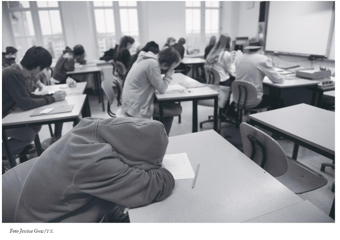 Ett klassrum med barn där ett barn sitter med huvudet nedsjunket på skolbänken.